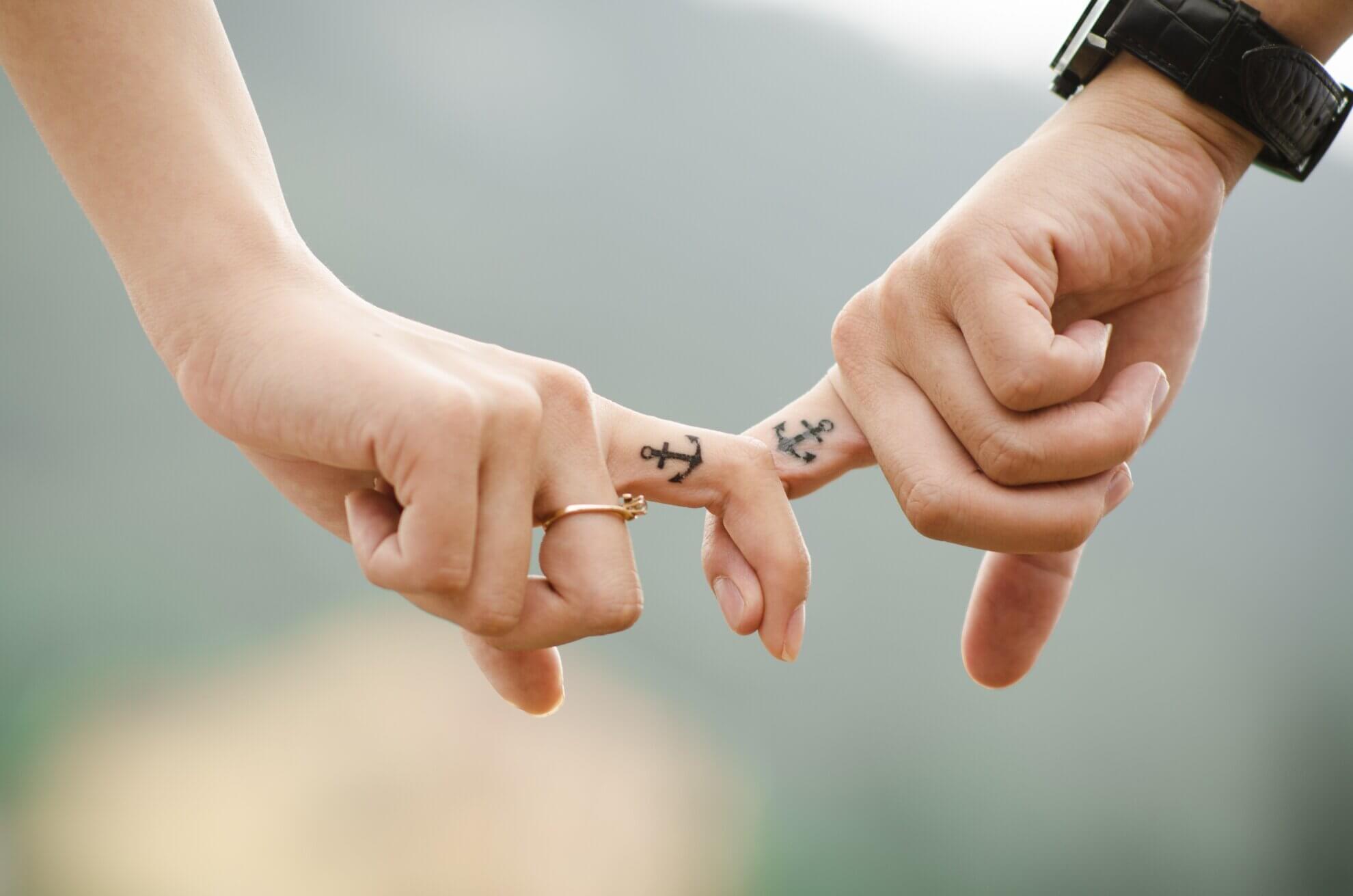 Zwei Hände halten sich gegenseitg mit den Zeigefingern, die mit Ankern tätowiert sind. Dies Bild dient als Symbol für eine freie Trauung.